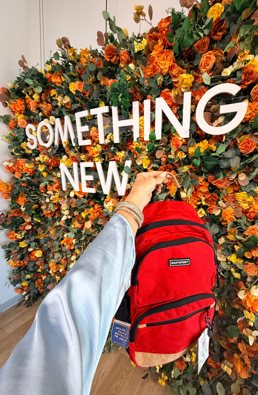 A person holding a red backpack in front of a floral wall with the words 