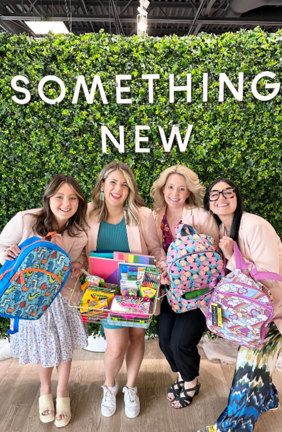 Four women standing in front of a greenery backdrop with the words 